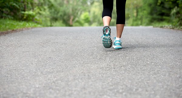 Eine Frau joggt auf einem asphaltierten Weg, zu sehen sind nur ihre Unterschenkel und Füße
