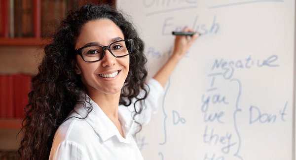 Eine junge Frau mit Locken schreibt Englischvokabeln auf ein Whiteboard und lächelt dabei in die Kamera