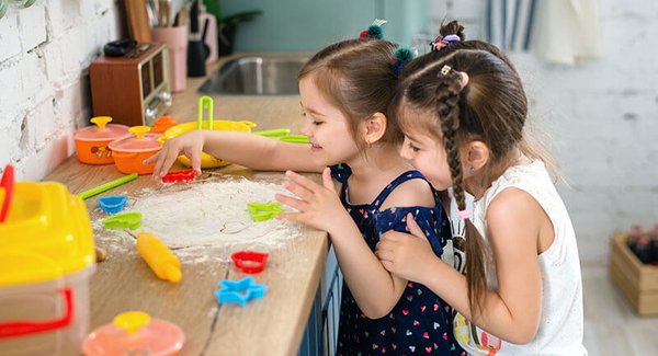 Zwei kleine Mädchen stechen in der Küche Plätzchen aus