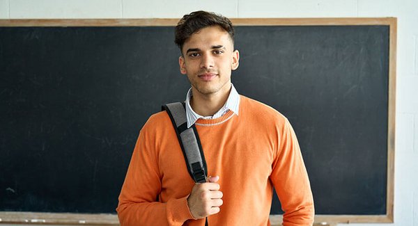 Junger Mann mit Rucksack steht vor einer Tafel