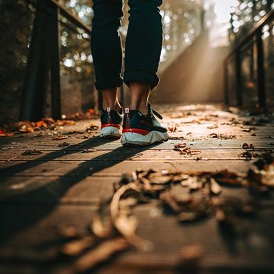 Eine Person geht über eine Brücke mit Herbstlaub, man sieht nur die Beine.