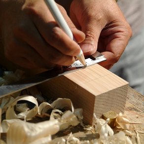 Auf einem Holzstück wird mit einem Bleistift ein Maß angezeichnet