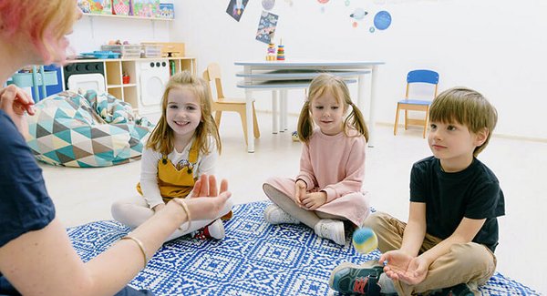 Eine Erzieherin sitzt mit drei kleinen Kindern im Sitzkreis