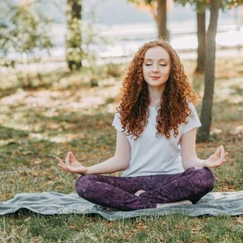 Frau sitzt in Yoga-Pose auf einer Wiese.