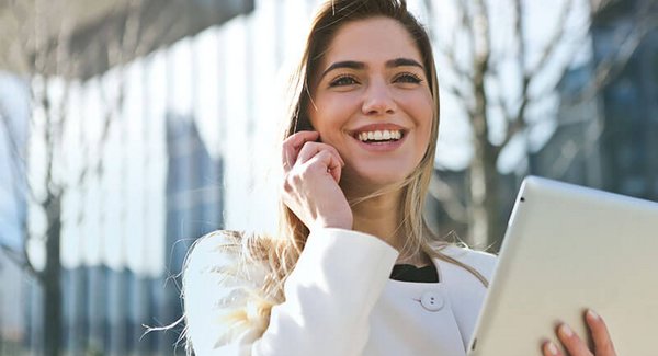 Junge blonde Frau mit einem Tablet in der Hand telefoniert mit einem Smartphone