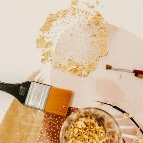 Blattgoldpartikel und Pinsel liegen auf einem Tisch
